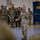 Leapfest 2026 (Pre Jump Training) A U.S. Army officer is addressing a group of multinational military personnel in what appears to be a hangar or large indoor military facility. The speaker is holding a microphone and gesturing while speaking to a crowd of soldiers wearing various camouflage uniforms. The setting suggests a briefing, ceremony, or multinational training event.