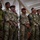 Leapfest 2026 (Pre Jump Training) A group of military personnel from multiple nations are standing together in an indoor facility, appearing to attend a briefing or formation. The soldiers are wearing various camouflage uniforms and insignia suggesting a multinational military exercise or joint operation. One soldier is notably wearing a maroon/red beret, indicative of airborne or paratrooper units.