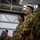 Leapfest 2026 (Pre Jump Training) A group of military personnel standing in formation inside what appears to be a hangar or large indoor facility. The soldiers in the foreground are wearing Canadian Armed Forces CADPAT (Canadian Disruptive Pattern) uniforms, with a Canadian flag patch clearly visible on one soldier's shoulder. A soldier on the far right is wearing a different camouflage pattern, suggesting a multinational or joint military event.