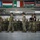 Leapfest 2026 (Pre Jump Training) Military personnel from multiple nations are gathered inside a large hangar facility, likely during a multinational training exercise or briefing. Several soldiers in the foreground are holding yellow static lines or ropes, suggesting a parachute or airborne operations training context. The presence of international flags and diverse camouflage patterns indicates a coalition or joint military event.