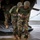 Leapfest 2026 (Pre Jump Training) Military personnel wearing camouflage uniforms with what appears to be Kenyan flag patches are boarding or exiting a military helicopter via its rear ramp. Two soldiers in the foreground appear to be assisting or steadying each other near the ramp. The setting appears to be a wet tarmac or airfield under overcast conditions.