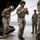 Leapfest 2026 (Pre Jump Training) Military personnel in multicam camouflage uniforms are gathered near the rear ramp of a large military helicopter or transport aircraft on a tarmac. Several soldiers appear to be conducting pre-mission or post-mission equipment checks, with two wearing helmets with netting. The setting appears to be an airfield under overcast skies.