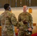 Two U.S. Air Force personnel in OCP (Operational Camouflage Pattern) uniforms are engaged in conversation inside what appears to be a military chapel. The servicemember facing the camera has a name tape partially readable as 'CLARK' and 'U.S. AIR FORCE' tape visible, and is holding a patrol cap in his hand. The setting features wooden pews with red cushions and stained glass windows, consistent with a military base chapel.