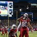 An NFL preseason game featuring the Arizona Cardinals celebrating what appears to be a touchdown near the end zone. Player #80 Fehoko is being lifted by a teammate in celebration, while #28 in an Arizona jersey looks on. The scoreboard in the background indicates a Hall of Fame Game, with game statistics visible on the display.