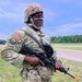 A U.S. Army soldier stands outdoors on a grassy training area wearing full Operational Camouflage Pattern (OCP) uniform and combat helmet. The soldier is holding an M16-style rifle with a yellow training muzzle cap attached, indicating a training exercise. Visible patches and name tape suggest an active-duty or National Guard affiliation.