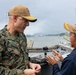 Two military personnel are engaged in conversation aboard what appears to be a naval vessel transiting through a canal lock, likely the Panama Canal. The individual on the left wears U.S. Marine Corps MARPAT camouflage uniform with the name tape 'DONOVAN' and three-star rank insignia indicating a Lieutenant General. Both individuals wear matching tan/coyote brown baseball caps with yellow insignia.