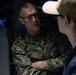 A U.S. Marine Corps officer with the name tape 'DONOVAN' is engaged in conversation in a dimly lit environment. He is wearing MARPAT camouflage uniform with general officer rank insignia (four stars visible on collar). He appears to be speaking with another individual whose back is partially visible in the foreground.