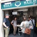 A group of four to five individuals are gathered at the entrance of an Air Force M.E.U. 01 (Mobile Embalming Unit), appearing to receive a briefing or tour of the facility. The unit displays the Air Force Mortuary Affairs Operations shield/crest on its signage. The interior shows stainless steel equipment, shelving, and a wheeled gurney or table.