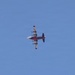 A firefighting aircraft is photographed from below against a clear blue sky. The plane is red and white with 'COULSON' visible on one wing and 'FIRE' on the tail, identifying it as a Coulson Aviation air tanker used for aerial firefighting operations. The image is taken from a ground-level perspective looking upward.