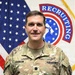 A U.S. Army officer in Operational Camouflage Pattern (OCP) uniform poses for an official portrait photo. The name tape reads 'JOHNSON' and the rank insignia on the chest pocket indicates the rank of Major (O-4), denoted by the black oak leaf cluster. The background features the U.S. flag and a U.S. Army Recruiting Command guidon/flag.