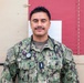 A U.S. Navy service member named Talavera is photographed in a portrait-style image wearing Navy Working Uniform (NWU) camouflage. The individual has a stethoscope around their neck and a rank insignia on their chest, indicating a medical officer role. They are standing in front of what appears to be a military medical vehicle or container marked with a red cross symbol.
