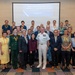 A formal group photograph taken at a Daniel K. Inouye Asia-Pacific Center for Security Studies (DKI APCSS) program event in Hanoi, dated August 5, 2026. The gathering includes military personnel, civilian officials, and program participants posing in front of a presentation screen displaying the DKI APCSS program title. The event appears to be a multilateral security studies conference or workshop with international attendees.