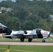 A Soviet-era MiG-17 (or Chinese J-5 variant) jet fighter painted in a black-and-white camouflage scheme with the number '511' in red on the fuselage is taxiing or taking off on a runway. The aircraft displays a red star insignia on the tail fin and bears the FAA registration 'N6963X', indicating it is a privately operated warbird in the United States. The background shows motion blur consistent with a panning camera technique, with trees and residential structures visible beyond the airfield.