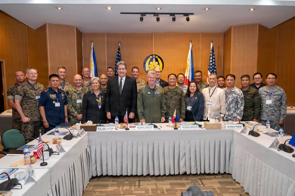 A formal group photo of approximately 20 military and civilian officials gathered in a conference room, with both Philippine and American flags visible in the background along with an official seal. Name placards on the conference table identify key participants including H.E. Lee Lipton, ADM Samuel J. Paparo (USN), GEN Antonio G. Navarrete (PN), and ASEC Monita B. Rodriguez. The setting suggests a bilateral military or defense cooperation meeting between the United States and the Philippines.