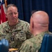 A U.S. Navy officer with the name tape 'CIEREWKO' and rank insignia of a Vice Admiral (three stars) is engaged in conversation with other military personnel at what appears to be a formal meeting or briefing. He is wearing the Navy Working Uniform (NWU Type III) with a Naval Aviator badge and 'U.S. NAVY' tape visible. An American flag and what appears to be a command flag are visible in the background.