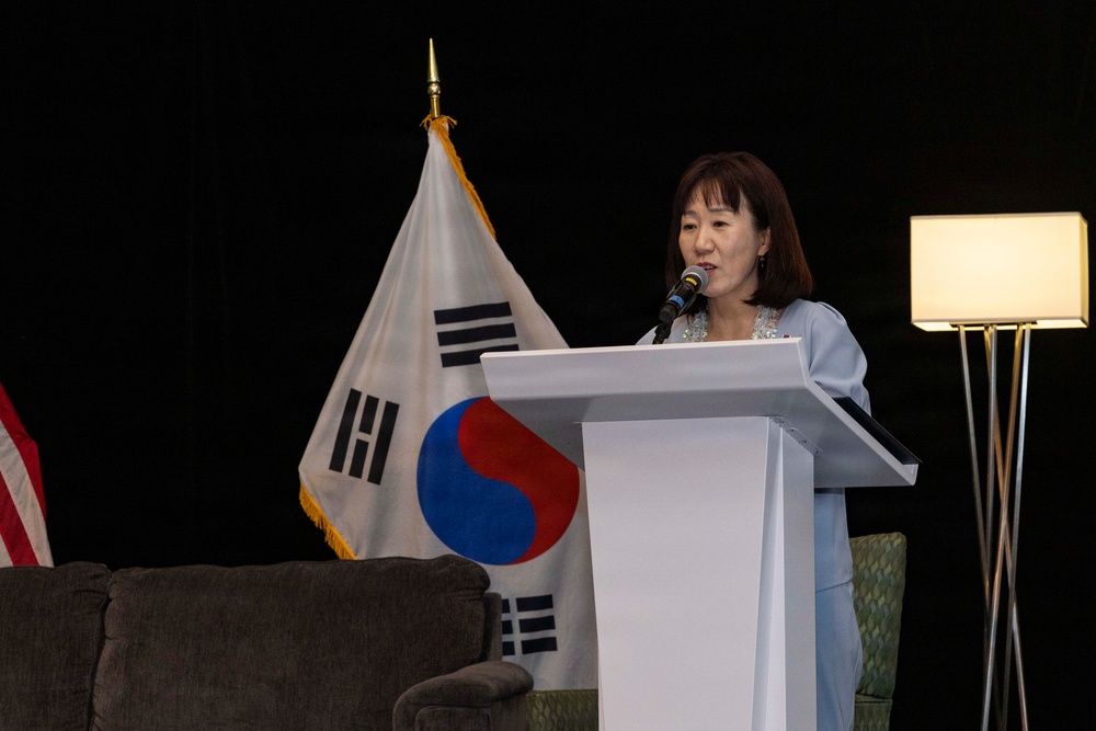 A woman is speaking at a white podium with a microphone at what appears to be a formal event or ceremony. The South Korean flag (Taegukgi) is prominently displayed behind her, along with what appears to be a partial view of the American flag on the left side. The setting suggests a bilateral or diplomatic event between South Korea and the United States.