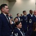 A formal military ceremony or banquet featuring U.S. Air Force personnel in dress blue uniforms with bow ties. Multiple enlisted members are standing at attention in a banquet hall setting, with some civilians seated at tables. The rank insignia visible on uniforms indicates Technical Sergeant and Master Sergeant grades among the attendees.