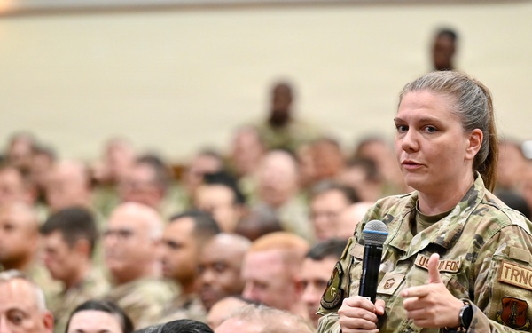 A large gathering of U.S. Air Force personnel in a auditorium or assembly hall setting. A female service member is standing and speaking into a microphone, likely during a question-and-answer session or all-hands meeting. The audience consists of hundreds of uniformed military personnel seated in rows.
