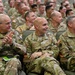A large group of military personnel in OCP (Operational Camouflage Pattern) uniforms are seated in an auditorium or briefing room, appearing engaged and smiling. The front row includes individuals with visible name tapes reading 'ADKINS,' 'SICILIANO,' and 'EIKENBERRY,' representing both U.S. Army and U.S. Air Force personnel. The atmosphere appears relaxed and positive, suggesting a formal but lighthearted military gathering or ceremony.