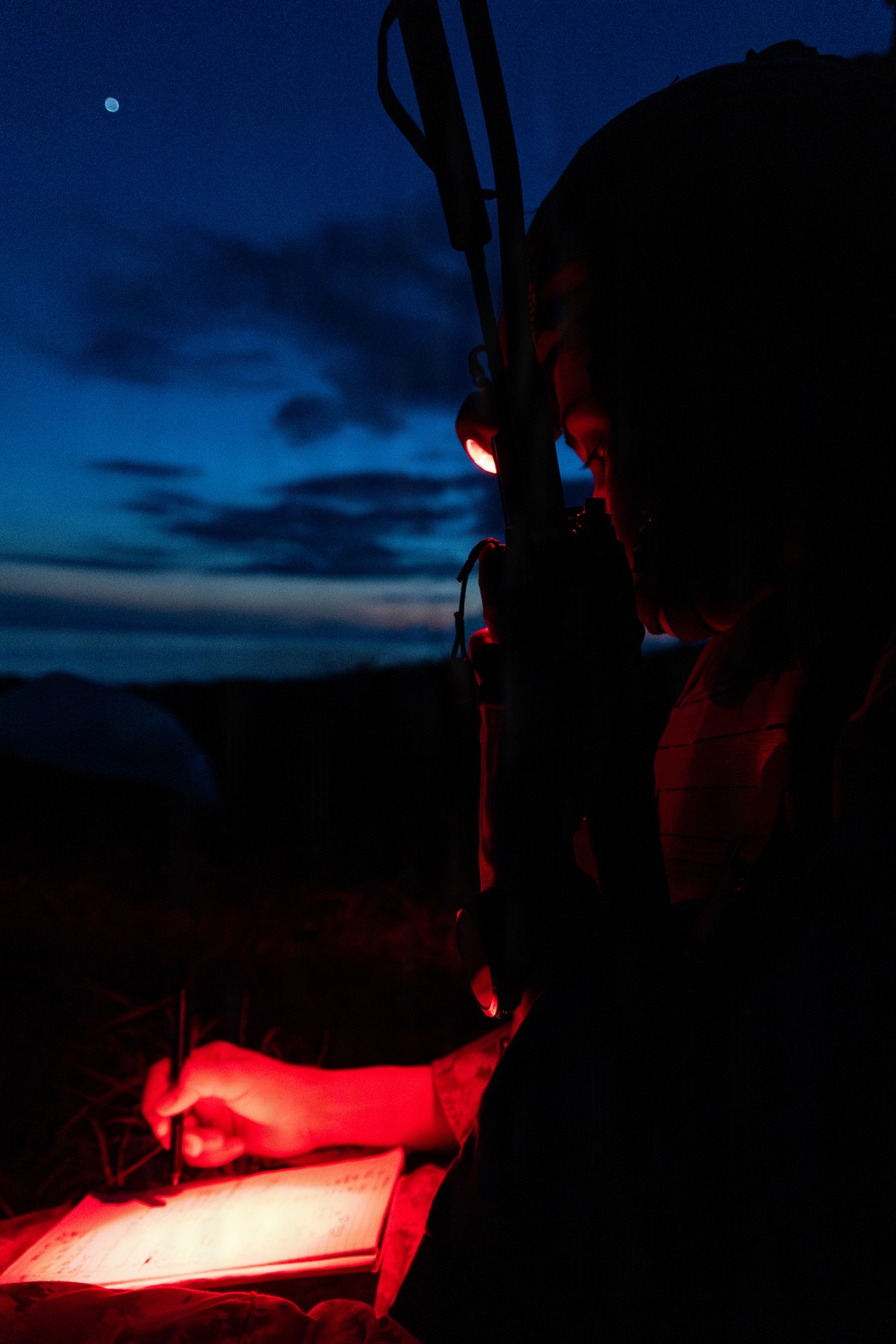 A person is writing in a notebook or document outdoors at night, illuminated by a red light source attached near their head. A rifle or long firearm is visible slung over their shoulder or back. The scene is set against a twilight sky with visible clouds and a moon in the upper left corner.