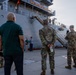 Military personnel and civilians are gathered on a dock in front of a large gray vessel named 'Gen. Brehon B. Somervell.' The group appears to be attending a formal dockside event or briefing near the ship's gangway. Multiple soldiers in OCP (Operational Camouflage Pattern) uniforms are present alongside civilians in casual attire.