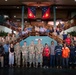 A large group photo taken inside a building featuring military personnel in camouflage uniforms, civilian workers in high-visibility safety gear, and officials posing across multiple levels of a staircase. The Papua New Guinea national flag is prominently displayed in the background, suggesting this is an official or governmental venue in PNG. The gathering appears to represent a multinational or inter-agency collaboration involving military, humanitarian, and civilian organizations.