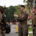 Three military personnel are engaged in a conversation outdoors in what appears to be a tropical environment. The individual on the left wears a different uniform with a cap bearing a Panamanian flag patch and carries a rifle, while the two on the right wear U.S. Marine Corps MARPAT camouflage uniforms. The interaction appears to be a coordinated discussion or briefing between allied forces.