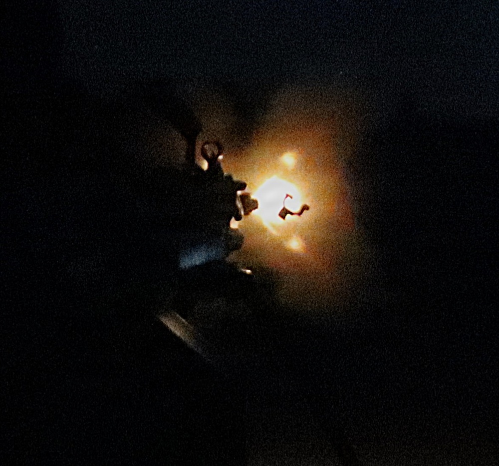 A very dark image showing a bright, intense light source at the center, surrounded by an orange-amber glow against an almost entirely black background. The light appears to emanate from or near a mechanical or structural object partially visible in silhouette. The high contrast between the bright core and the surrounding darkness makes detail identification difficult.