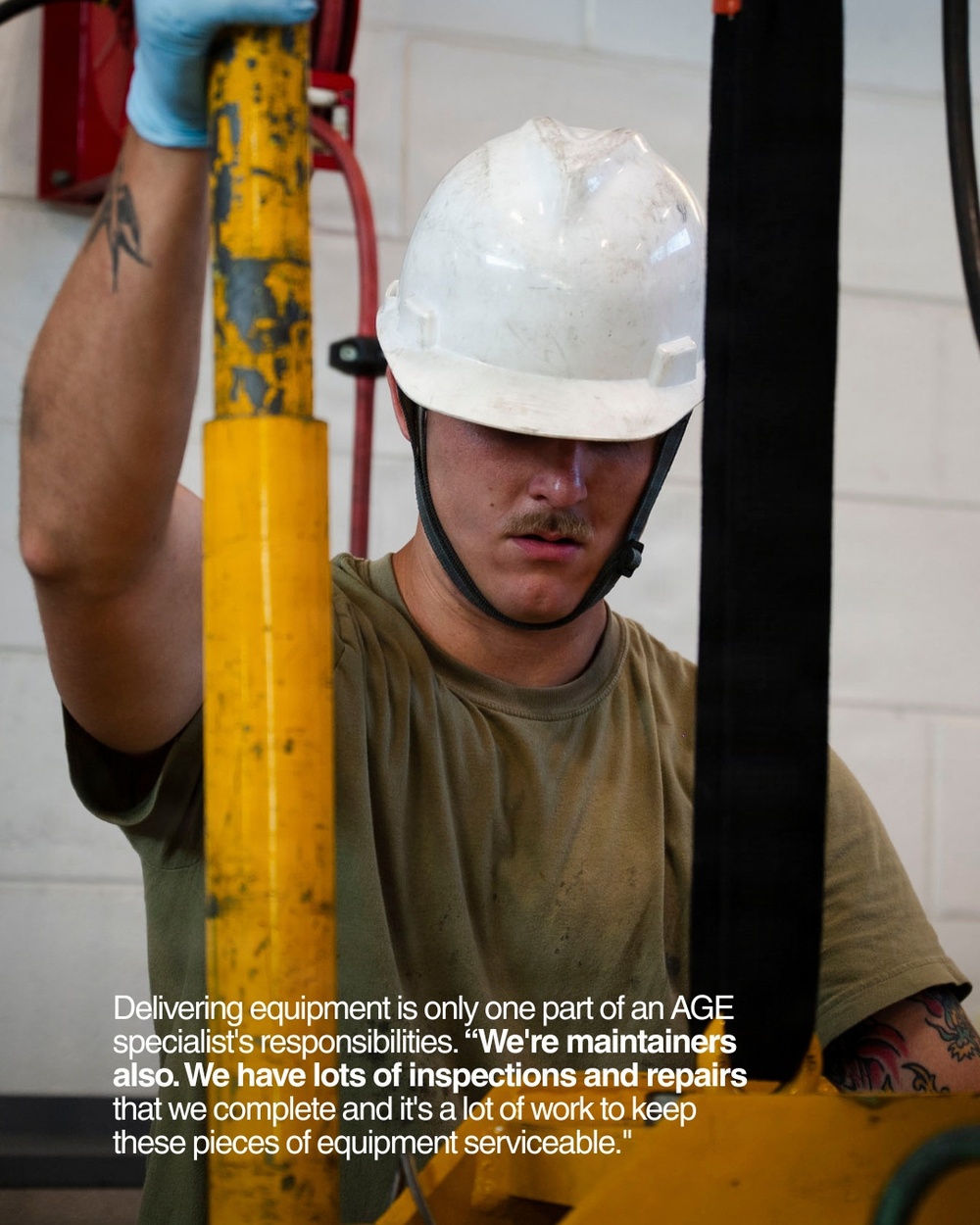 A young male worker wearing a white hard hat and olive green t-shirt is performing maintenance or inspection work on yellow industrial equipment. He is wearing a blue latex glove on his raised hand and has visible tattoos on both arms. The image is accompanied by a caption referencing AGE (Aerospace Ground Equipment) specialist responsibilities.