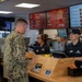Two military personnel in camouflage uniforms are ordering food at a fast food counter, likely located on a military base. Two employees in black uniforms and caps are serving them at the counter. The restaurant appears to be a combination of Pizza Hut and another chain, based on the visible menu boards.