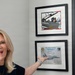 A blonde woman is enthusiastically pointing at two framed military aviation certificates/photos mounted on a wall. The frames appear to contain a photograph of someone in a fighter jet cockpit and a certificate from the 492d Fighter Squadron 'Madhatters'. An American flag is partially visible on the right side of the image.