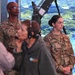 Two U.S. Army soldiers in OCP (Operational Camouflage Pattern) uniforms stand in what appears to be a broadcast or media studio environment. The soldier on the right has the name tape 'HILDEBRAND' and a captain's rank insignia, while the soldier in the background bears the name tape 'WRIGHT'. They appear to be observing a broadcast or media production in progress.