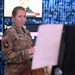 A female U.S. Army soldier in MultiCam (OCP) uniform stands in what appears to be a media or broadcast environment. She is wearing a 101st Airborne Division patch with Airborne tab on her left shoulder and an American flag patch, with a name tape reading 'SMITH'. She appears to be holding papers or a clipboard and looking toward the camera.