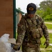 A U.S. Army Sergeant named Crockett, wearing OCP (Operational Camouflage Pattern) uniform with full tactical vest, is applying what appears to be a cryogenic or smoke-producing device to a metal object on a concrete surface. The soldier is assigned to the 787 EOD (Explosive Ordnance Disposal) unit, as indicated by the 'Sasquatches' patch on his cap. The activity appears to be an EOD training or operational procedure conducted outdoors near a building.