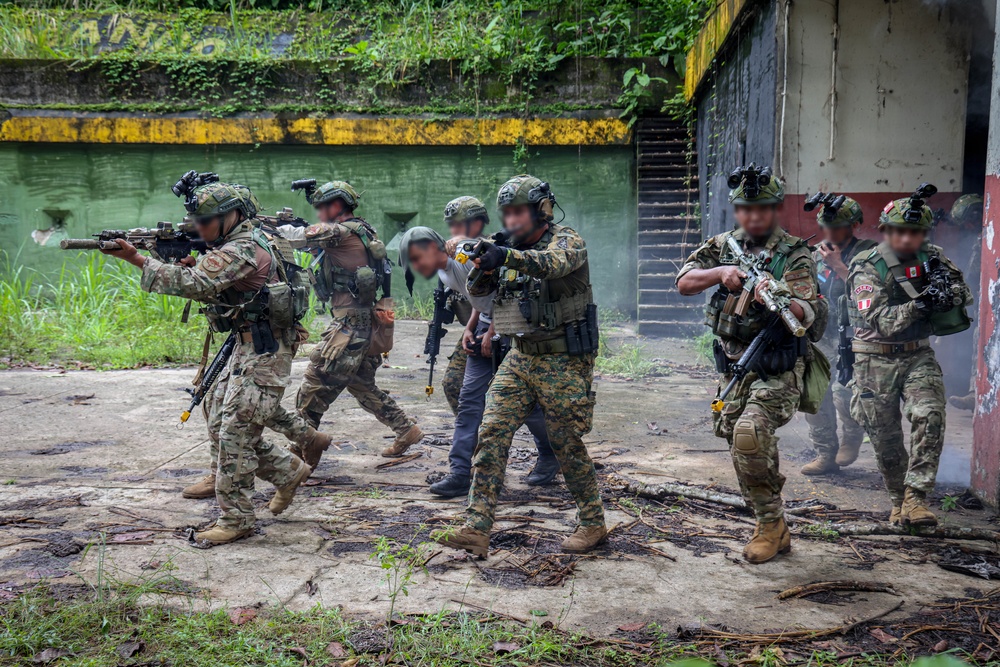 The image depicts a military or law enforcement tactical operation, likely a training exercise or live raid, in an outdoor urban-decay environment with tropical vegetation. Multiple armed personnel in varied camouflage uniforms are escorting what appears to be a detainee or role-player. At least one patch visible on a personnel member appears to be Peruvian, suggesting a multinational or joint operation context.
