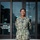 I Keep the Warfighter in the Fight: Hospital Corpsman Second Class Emmanuella Gbogbo A U.S. Navy enlisted service member in NWU Type III (green digital camouflage) uniform stands smiling in front of a military facility entrance. She is standing on a decorative floor mosaic bearing a naval unit insignia and the motto 'Not for Self But for Country.' The background glass doors display the phrase 'Keeping the Warfighter in the Fight.'