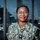 I Keep the Warfighter in the Fight: Hospital Corpsman Second Class Emmanuella Gbogbo A U.S. Navy service member wearing the Navy Working Uniform (NWU) stands in front of a building entrance with glass doors. The name tape reads 'GOGBO' and the rank insignia indicates a Petty Officer Third Class. The subject is smiling and posed for what appears to be an official or portrait-style photograph.