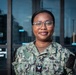 A U.S. Navy service member wearing the Navy Working Uniform (NWU) stands in front of a building entrance with glass doors. The name tape reads 'GOGBO' and the rank insignia indicates a Petty Officer Third Class. The subject is smiling and posed for what appears to be an official or portrait-style photograph.
