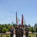 A formal U.S. Army military ceremony is taking place outdoors at what appears to be a memorial or parade ground. A central figure in Army Combat Uniform (ACU) is rendering a salute while flanked by color guard soldiers holding rifles at attention. The ground displays a unit insignia mat reading '3rd Brigade Engineer Battalion, 34th Infantry Division' with the word 'FORWARD' and a red and blue unit crest.