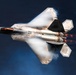 A high-performance stealth fighter jet, identifiable as an F-22 Raptor, is captured in a dramatic low-altitude maneuver against a dark blue sky. The aircraft is photographed from above at an angle, with afterburners ignited and visible vapor condensation forming around the fuselage, indicating high-speed, high-G flight. The image showcases the aircraft's distinctive angular stealth geometry and twin engine exhaust plumes with visible flame.