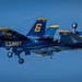 The image shows multiple U.S. Navy Blue Angels F/A-18 Hornet jets flying in extremely close formation against a clear blue sky. The aircraft display their iconic navy blue and gold color scheme with visible aircraft numbers 5 and 6, along with 'Blue Angels' and 'U.S. Navy' markings. Landing gear appears to be deployed on at least one aircraft, suggesting a low-speed airshow maneuver.