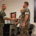 Several military personnel in MARPAT (Marine Pattern) camouflage uniforms are gathered in what appears to be a briefing or conference room. Two individuals in the foreground are shaking hands in what appears to be a formal recognition or greeting ceremony, while two others observe in the background. The setting suggests an official military function such as an award presentation, promotion, or unit ceremony.