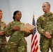 Three U.S. Army soldiers in MultiCam (OCP) uniforms stand before an American flag during what appears to be a formal military ceremony. The central soldier, identified by name tape as 'GORE,' is reading from a document while the soldier on the left (MOORE) holds a pen and the soldier on the right (METZ) stands at ease. The presence of a document, flag, and formal posture suggests this is a promotion, award, or oath-of-office ceremony.