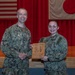 Two U.S. Navy personnel in NWU Type III (digital camouflage) uniforms pose together holding a wooden award plaque on a stage. The plaque appears to be a 'Bluejacket of the Quarter' award presented to MASN Sydney Pattison. The setting appears to be a military installation in Japan, evidenced by the American and Japanese flags displayed on the red-curtained stage backdrop.