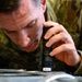A military service member in OCP (Operational Camouflage Pattern) uniform is closely inspecting a surface or component using a LuxPro brand flashlight. The individual is leaning in very close to examine what appears to be a piece of equipment or documentation. A red patch with the word 'EJECT' is visible on the uniform sleeve, suggesting possible aircrew or aviation maintenance association.