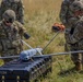 U.S. Army soldiers in MultiCam/OCP camouflage uniforms are preparing a fixed-wing UAV (unmanned aerial vehicle) in an open grassy field. The drone, marked with the number '113', is resting on a hard-shell transport case labeled '113A'. The soldiers appear to be conducting pre-launch assembly or inspection procedures.