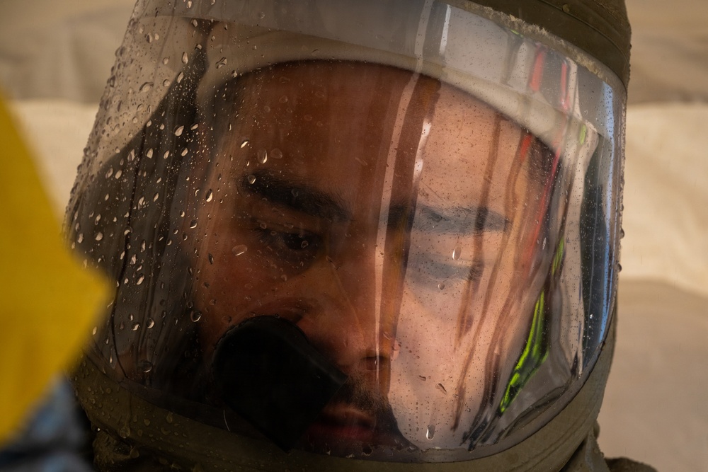A close-up photograph of a person wearing a protective helmet with a clear visor, which is covered in water droplets. The visor is fogged and wet, partially obscuring the face of the individual inside. Reflections of high-visibility markings or gear are visible on the visor surface.