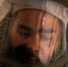A close-up photograph of a person wearing a protective helmet with a clear visor, which is covered in water droplets. The visor is fogged and wet, partially obscuring the face of the individual inside. Reflections of high-visibility markings or gear are visible on the visor surface.