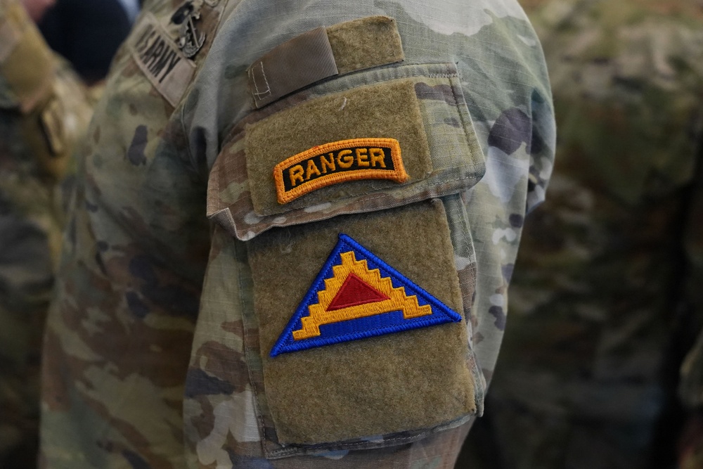 Close-up photograph of a U.S. Army soldier's left sleeve displaying two patches on a MultiCam (OCP) camouflage uniform. The upper patch is a Ranger Tab with gold lettering on a black background, and below it is the U.S. Army Central (ARCENT) shoulder sleeve insignia featuring a blue triangle with gold stepped border and red inner triangle. A 'U.S. ARMY' name tape is partially visible in the background on another soldier's uniform.