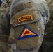 Close-up photograph of a U.S. Army soldier's left sleeve displaying two patches on a MultiCam (OCP) camouflage uniform. The upper patch is a Ranger Tab with gold lettering on a black background, and below it is the U.S. Army Central (ARCENT) shoulder sleeve insignia featuring a blue triangle with gold stepped border and red inner triangle. A 'U.S. ARMY' name tape is partially visible in the background on another soldier's uniform.